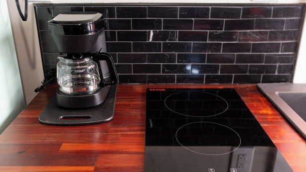 A kitchen with a black coffee maker on a glass carafe and a black induction cooktop. - Cozy Starkville Cottage — 4 Peaceful Acres + Pet Friendly (Starkville)