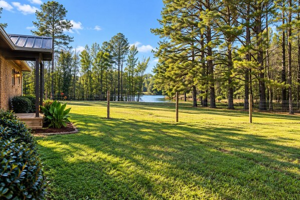 A well-maintained lawn with a wooden deck, a fenced area, and tall pine trees.