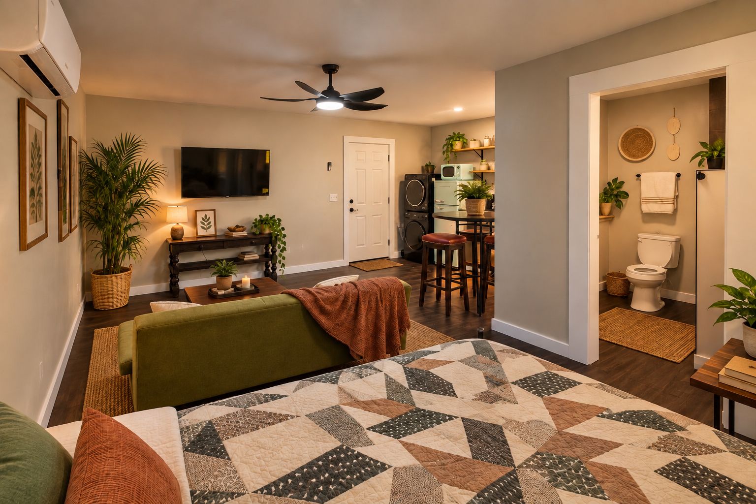 Un salon avec un canapé vert, un tapis à motifs, un ventilateur de plafond et un téléviseur fixé au mur.