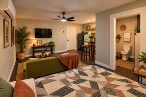 Ein Wohnzimmer mit einem grünen Sofa, einem gemusterten Teppich, einem Deckenventilator und einem an der Wand montierten Fernseher.