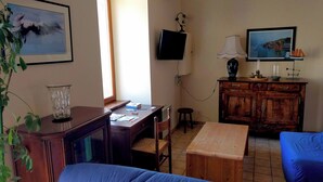 Ein Wohnzimmer mit einem Holztisch, einem an der Wand befestigten Fernseher, einem blauen Sofa und einem Holzschrank.