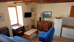 Ein gemütliches Zimmer mit einer Couch, einem blauen Sessel, einem kleinen Tisch, einer Holzkommode, einem Fernseher und einer Küchenzeile mit Kühlschrank und Mikrowelle.