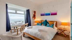 Habitación de hotel con una cama grande, vista al mar, una silla y obras de arte en la pared.