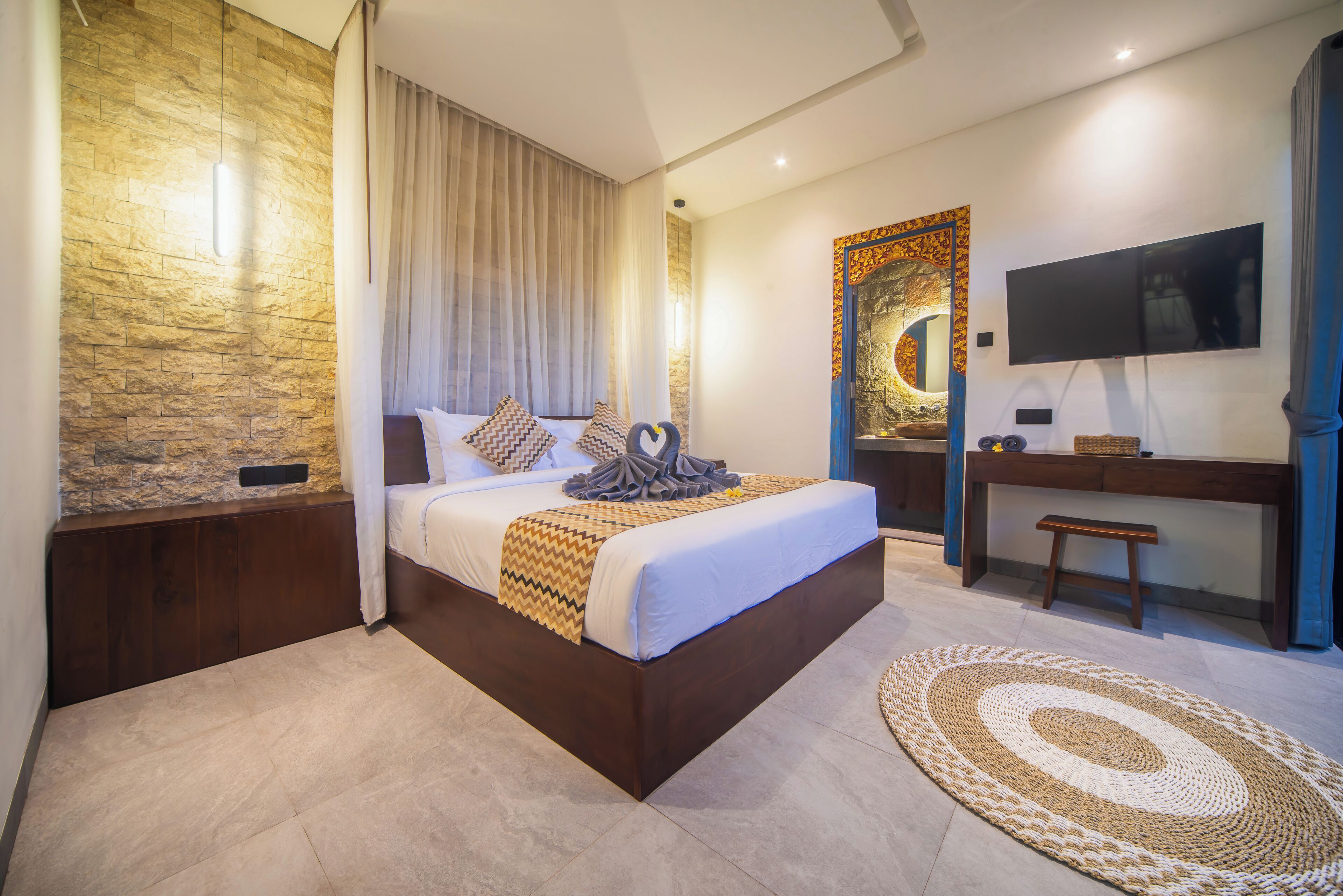 A modern bedroom with a large bed, a desk, a flat-screen TV, and a decorative wall piece.