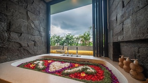 A bathroom with a stone wall, a window, a sink with a heart-shaped flower arrangement, and a chair. - 3Bedroom-703-Private Pool Villa Sanur (Denpasar)