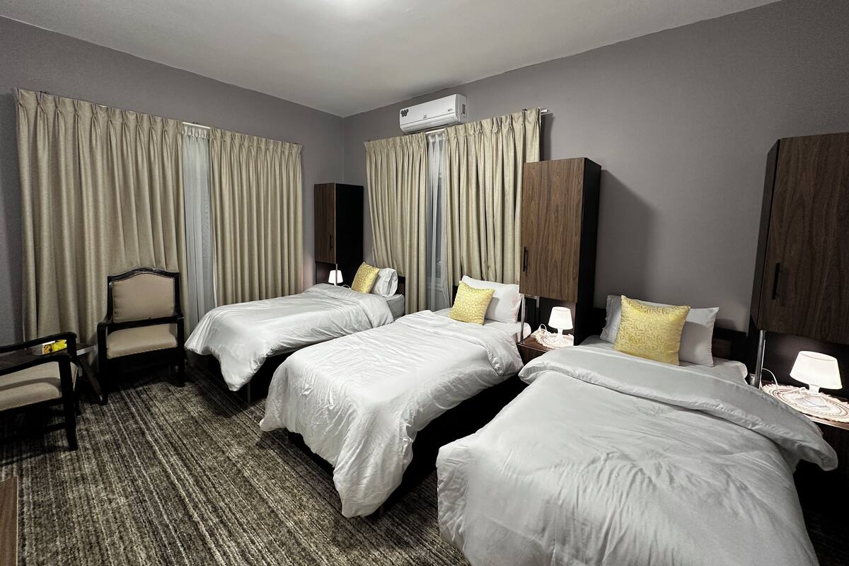 Ein Hotelzimmer mit zwei Einzelbetten, einem Sessel, einem Schreibtisch und einem Kleiderschrank.