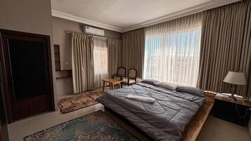 Ein Hotelzimmer mit einem großen Bett, einem Schreibtisch, einem Sessel, einem Fernseher und einem Fenster mit Vorhängen.