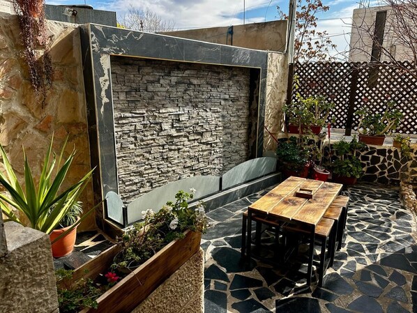 Eine Terrasse mit Steinmauer, Holztisch und Kübelpflanzen.