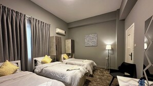 Habitació d'hotel amb dos llits, escriptori, cadira, aire condicionat, làmpada i una catifa estampada.