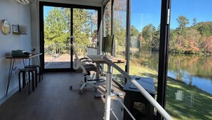 A room with a large window overlooking a lake, a treadmill, and a desk with a chair. - Hacker House - Do Your Best Work (LaGrange)