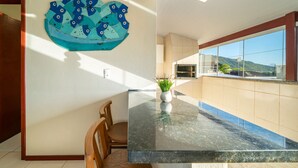 A modern kitchen with a large island, a decorative wall piece, and a view of the outdoors. - AP 16 Ala Tainha Residencial Solavir (Bombinhas)