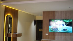 Une salle de bain moderne avec un meuble-lavabo en bois, un téléviseur fixé au mur qui diffuse une image de cascade, et un miroir doté d’un système d’éclairage original.