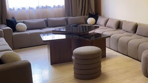 Un salon moderne avec un canapé d’angle, une table basse et un pouf rond.