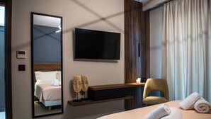 Ein Hotelzimmer mit Bett, Fernseher, Stuhl, Spiegel und einem Fenster mit Vorhängen.