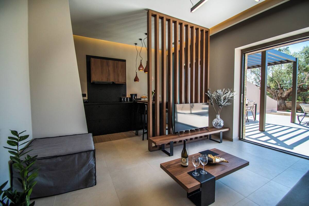 Un salon moderne avec un canapé, une table basse sur laquelle sont posés des verres à vin, un téléviseur et une porte coulissante donnant sur un balcon.
