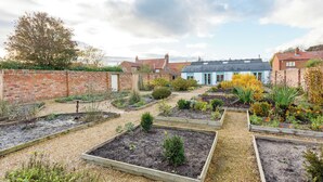A garden with raised beds, a brick wall, and a blue building in the background. - The Garden House in Low Catton (York)