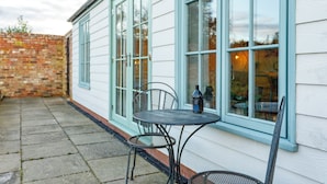 A patio with a table and chairs, a bottle, and a brick wall. - The Garden House in Low Catton (York)