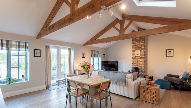 A spacious living area with a wooden dining table, comfortable seating, a fireplace, and a television. - The Garden House in Low Catton (York)