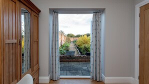A room with a wooden wardrobe, a white chair, and a view of a garden through a doorway. - The Garden House in Low Catton (York)