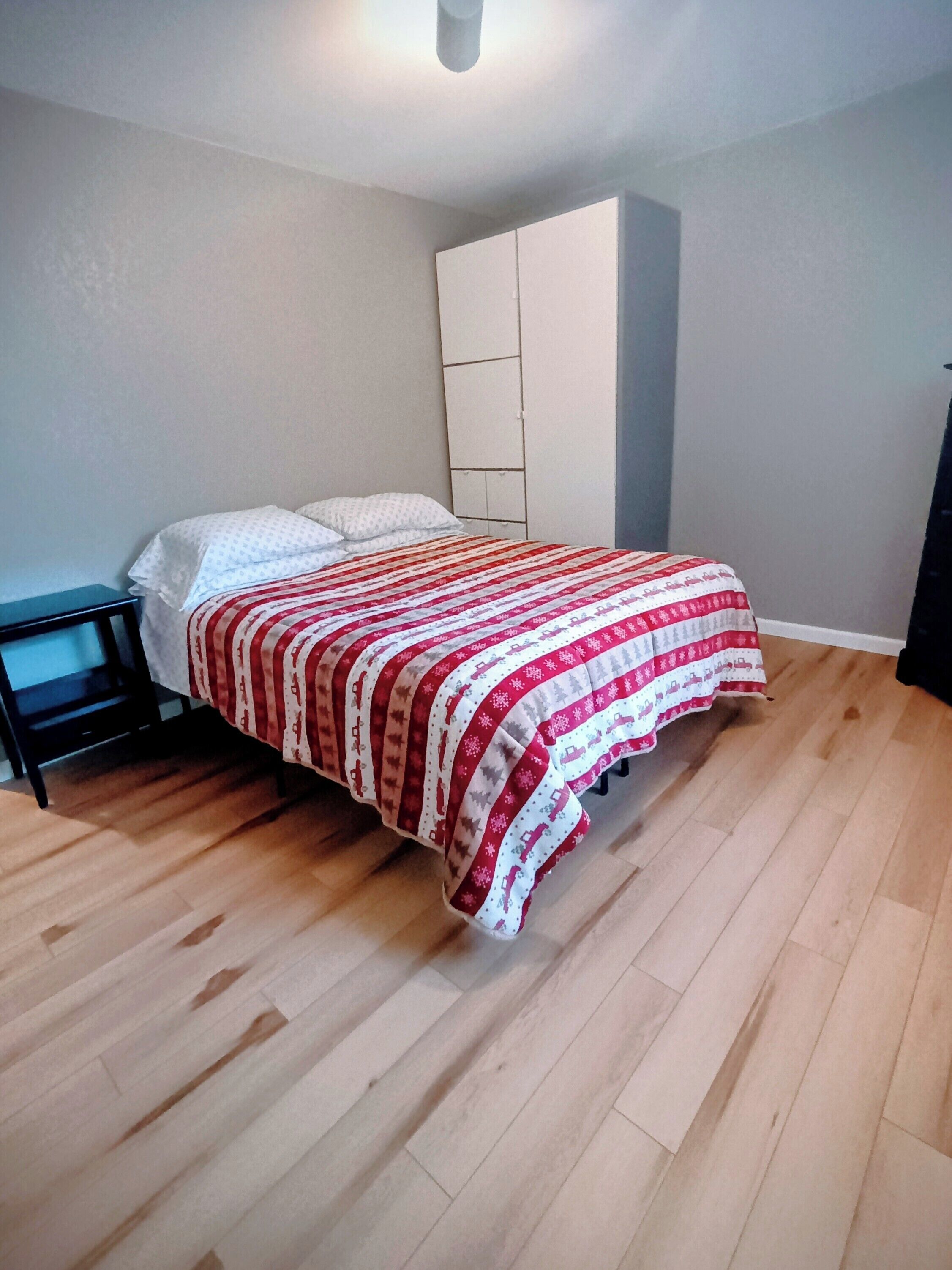 A bedroom with a bed, a nightstand, a wardrobe, and wooden flooring.
