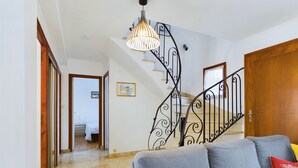 A living room with a grey sofa, a wooden door, and a staircase with a wrought iron railing. - Large family home 10 minutes from the beach (Fouesnant)