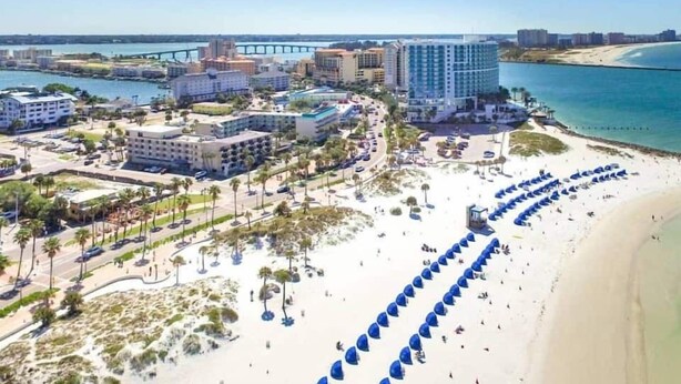Vista aérea de una zona turística costera con una playa, un puente y varios edificios, incluyendo un gran hotel.