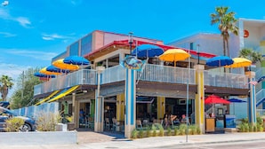 Un edificio de varios pisos con mesas al aire libre y sombrillas de colores.