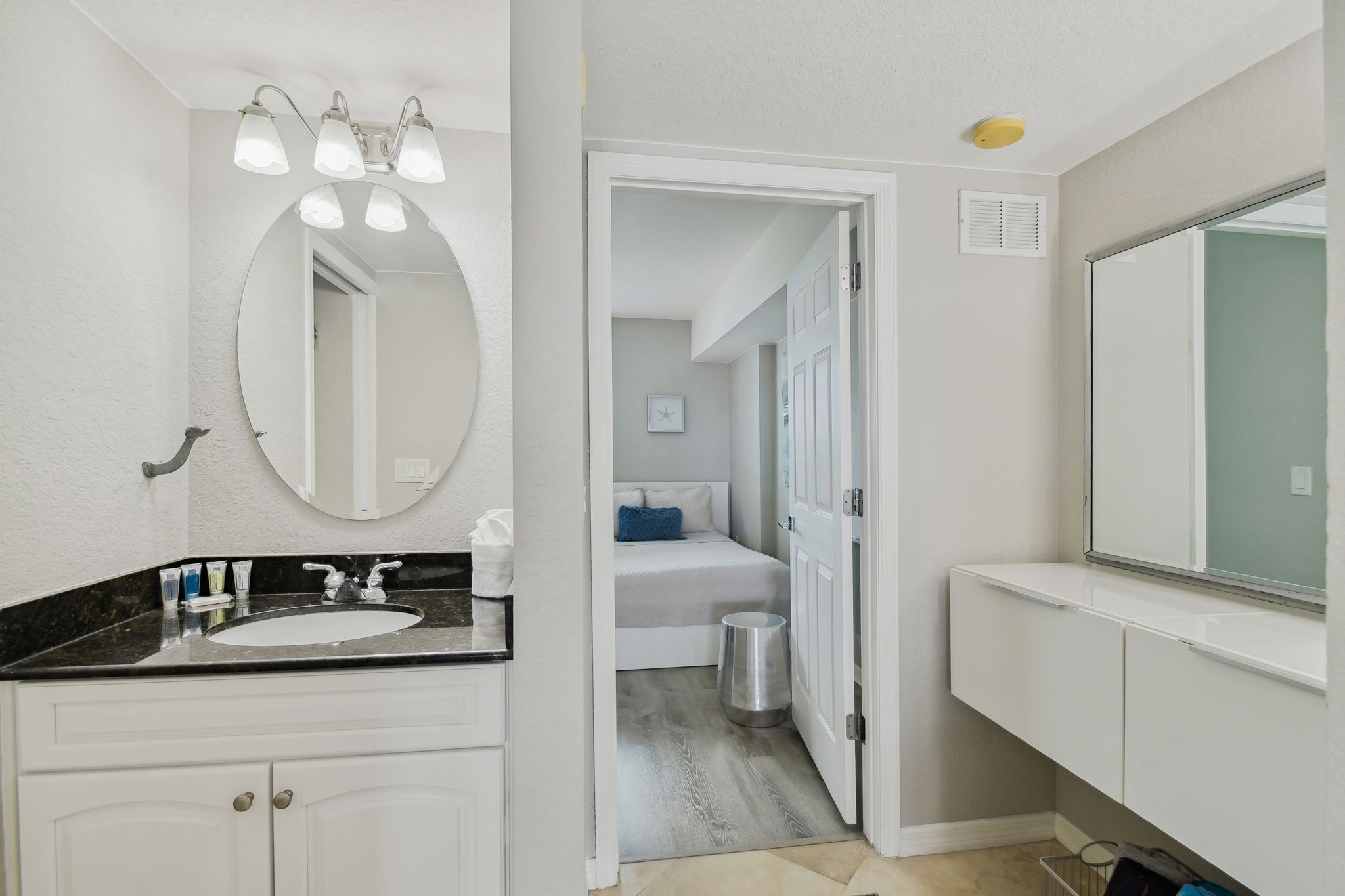 A bathroom with a white vanity, a round mirror, and a large mirror above the sink.