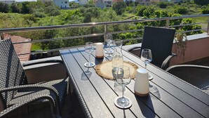 Een buiten eethoek met rieten stoelen en een tafel voor vier personen, met uitzicht op een woonwijk met huizen en begroeiing.