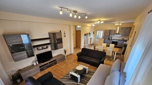 Een moderne woonkamer met een flatscreen televisie, donkere banken, een salontafel en een keuken op de achtergrond.