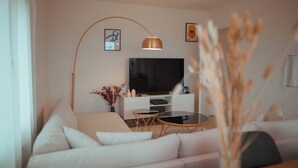 Una sala de estar moderna con un sofá blanco, una mesa de centro de vidrio, un televisor sobre un mueble blanco y una lámpara de pie.