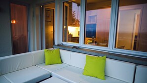 Un sofá blanco con dos cojines verde brillante, ubicado frente a una ventana con vista a una cocina.