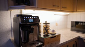 Una cafetera con pantalla digital, jarra de vidrio y un recipiente con muffins en una encimera de cocina.