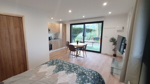 Une chambre à coucher moderne avec un lit, un coin repas comprenant une table et des chaises, une cuisine en arrière-plan et une grande porte-fenêtre coulissante donnant sur un patio.