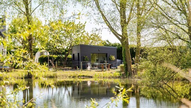 Une maison moderne située près d’un étang, avec un jardin clôturé et une serre.