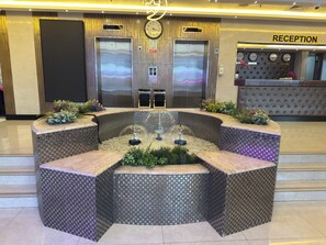 A reception area with a reception desk, two elevators, and a decorative water feature. - ORCHID HOTEL (Dubai)
