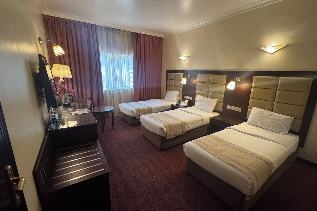 A hotel room with two beds, a desk, a chair, a lamp, and a window with curtains.