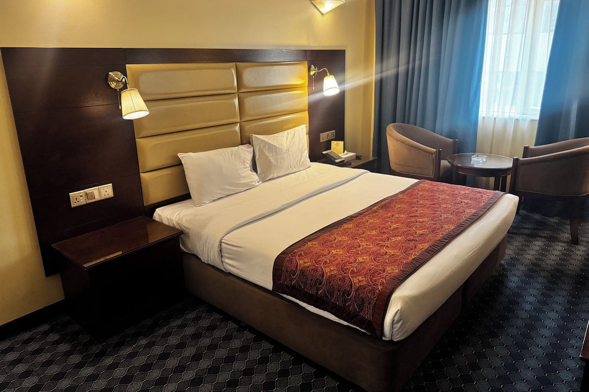 A hotel room with a large bed, bedside lamps, a desk, a chair, and a small table.