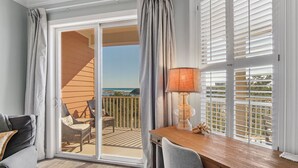 A balcony with a view of the ocean, wicker furniture, and a table with a lamp.