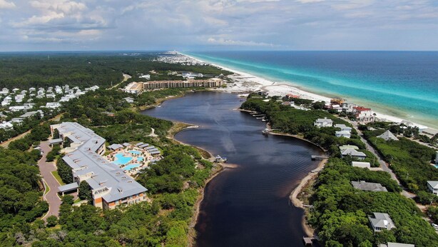 An aerial view of a resort with a large swimming pool, beachfront properties, and a marina.