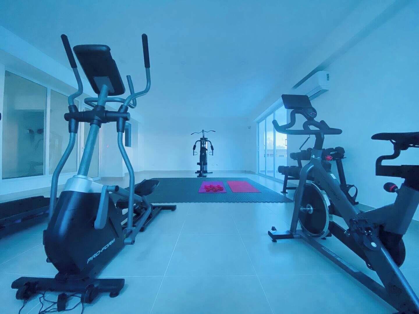 A gym with cardio machines, a stationary bike, and a yoga mat.