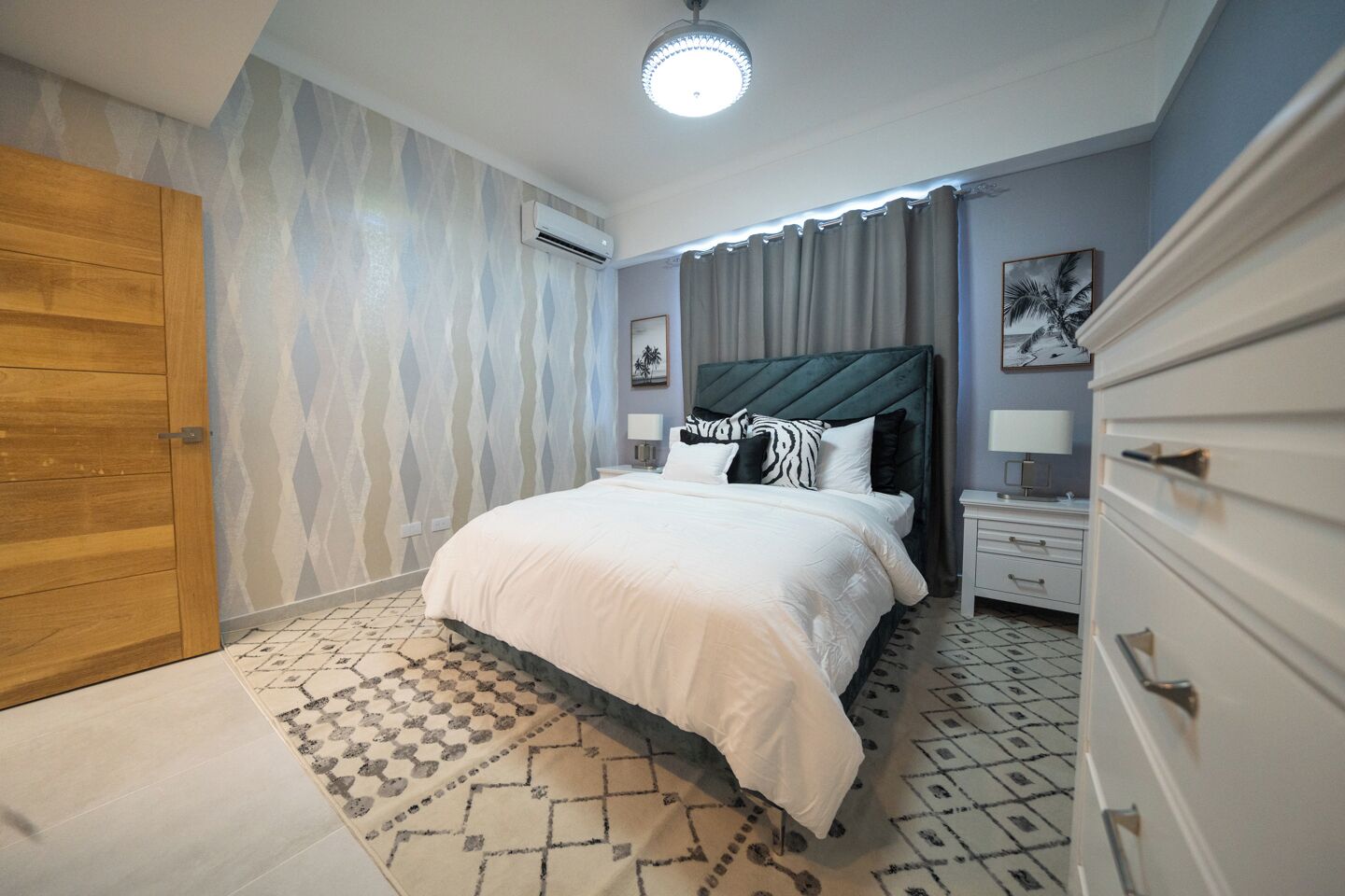 Ein Schlafzimmer mit einem Bett, Nachttischen, einer Kommode, einem gemusterten Teppich und einer Holztür.
