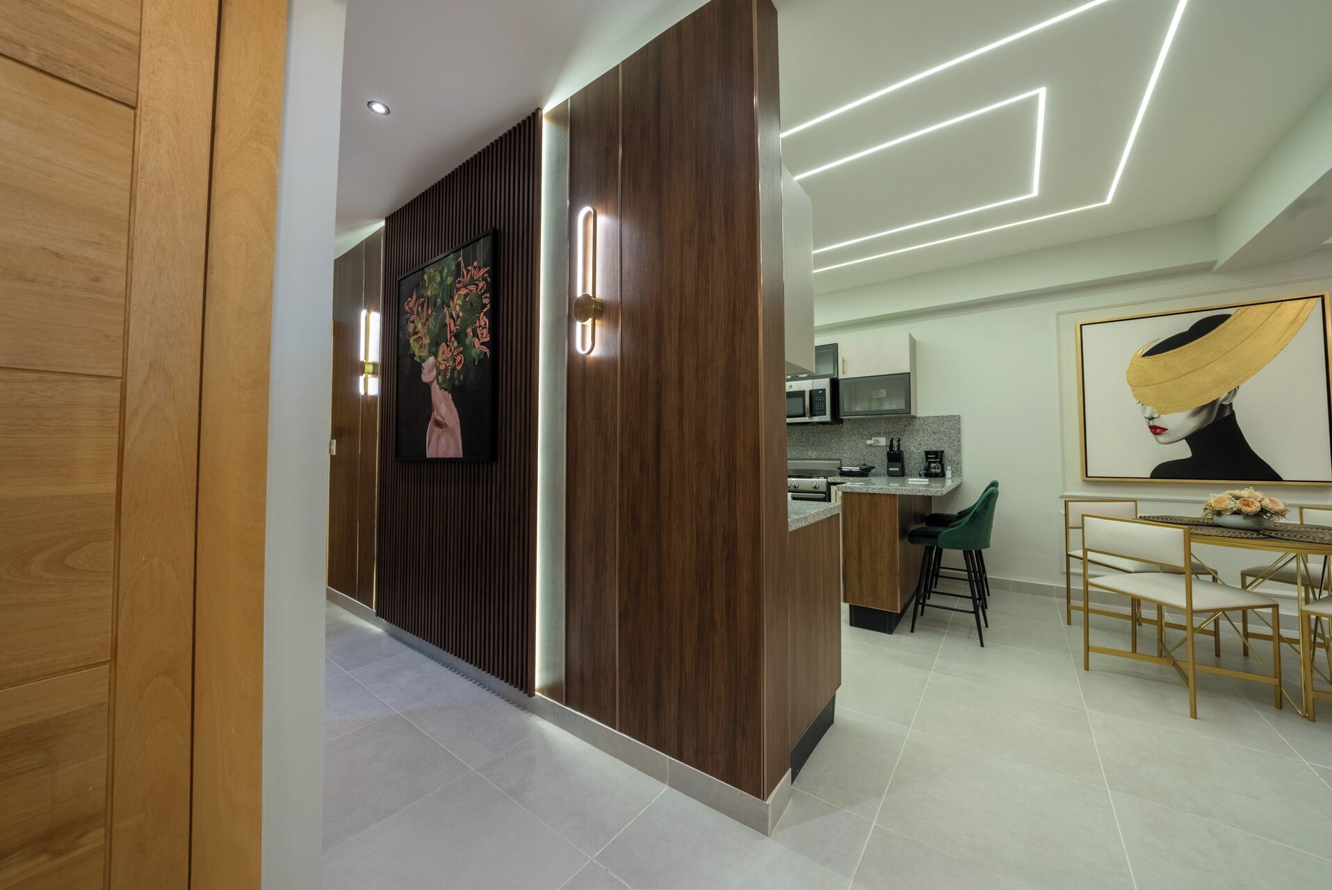 A modern kitchen with a central island, a dining area with a table and chairs, and a living space with a sofa and a painting.
