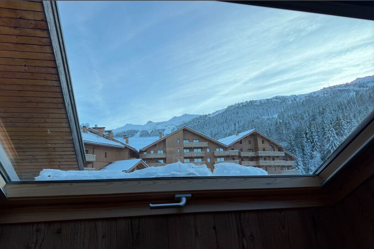 A view through a skylight of a chalet-style building with multiple balconies, surrounded by snow-covered trees and mountains.