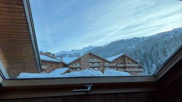 A view through a skylight of a chalet-style building with multiple balconies, surrounded by snow-covered trees and mountains.