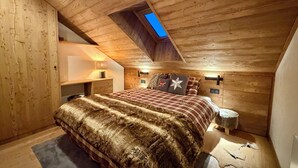 A cozy attic bedroom with a sloped ceiling, a skylight, a bed with a fur throw, and a nightstand with a lamp. - Troillet 11, 200m away from the ski pistes (Les Allues)