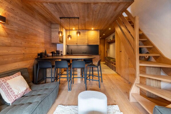 En mysig stuga med träpanel på väggarna, en soffa, en matplats och en trappa.