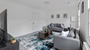 Ein modernes Wohnzimmer mit einem grauen Sofa, einem dunklen Holztisch und einem großen Flachbildfernseher.