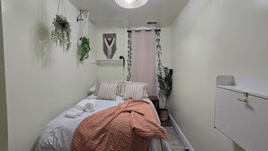 A small, neatly arranged bedroom with a bed, bedside plants, a hanging light fixture, and a white wardrobe.
