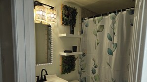 A bathroom with a white sink, a mirror with LED lights, a toilet, and a shower curtain with a leaf pattern.